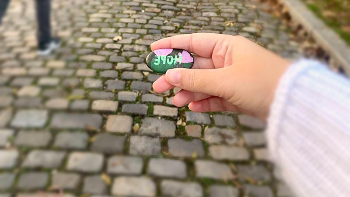 在欧洲的一条鹅卵石街道上，一个女孩拿着一块上面写着“希望”的石头